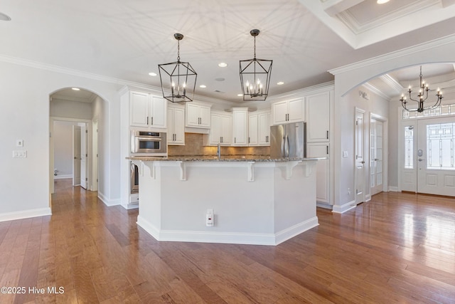 kitchen featuring white cabinetry, appliances with stainless steel finishes, decorative light fixtures, and dark stone countertops