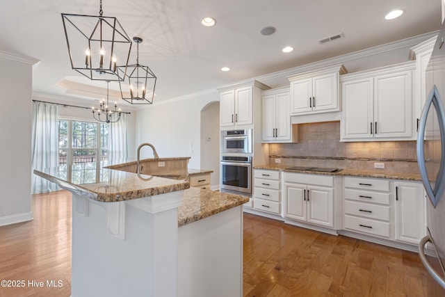 kitchen with hanging light fixtures, white cabinetry, sink, and a center island with sink