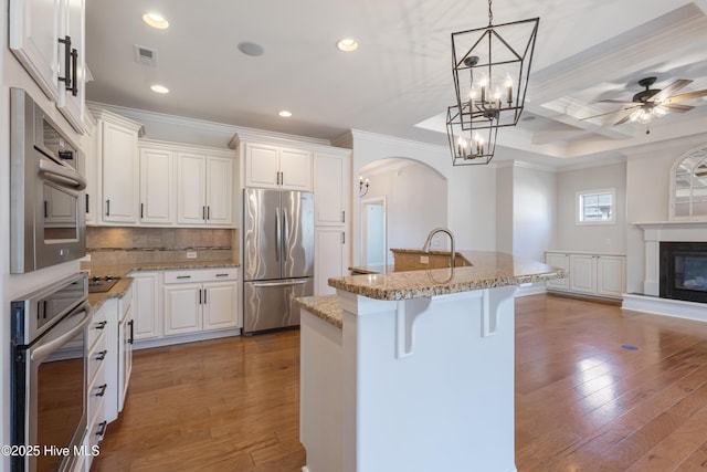 kitchen featuring white cabinets, an island with sink, stainless steel fridge, and a kitchen bar