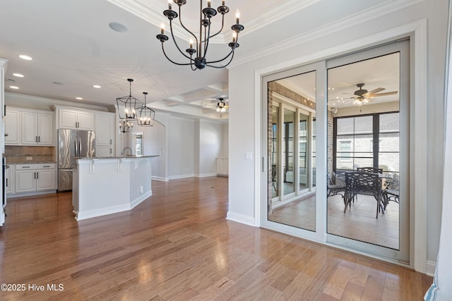 kitchen with white cabinetry, decorative light fixtures, a center island with sink, light hardwood / wood-style flooring, and stainless steel fridge