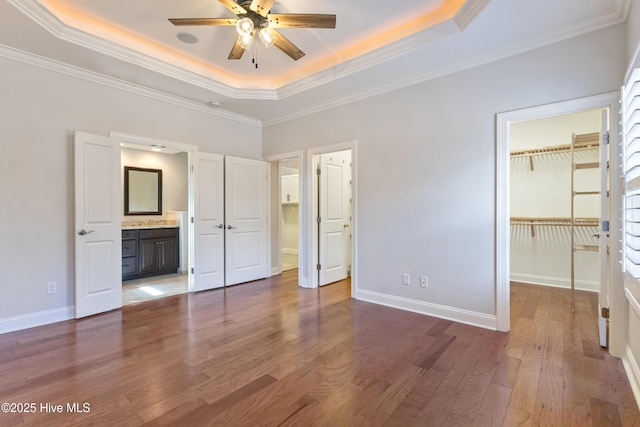 unfurnished bedroom with dark wood-type flooring, a walk in closet, a tray ceiling, and crown molding