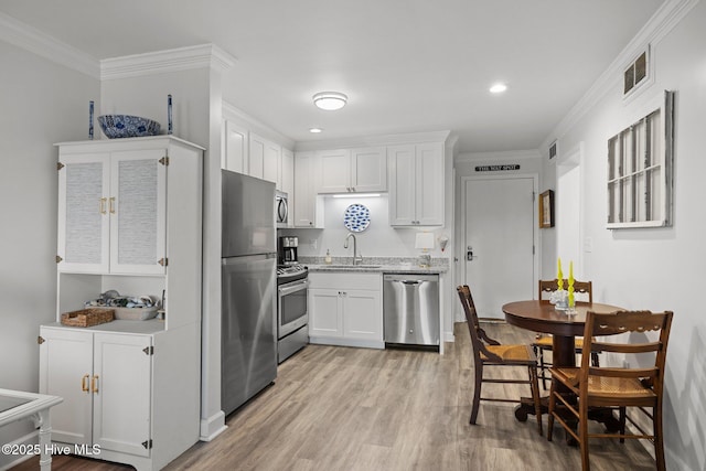 kitchen with a sink, visible vents, white cabinets, appliances with stainless steel finishes, and crown molding