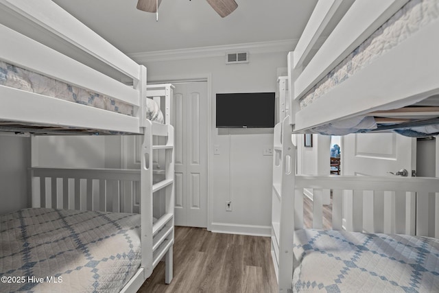 bedroom featuring ceiling fan, visible vents, crown molding, and wood finished floors