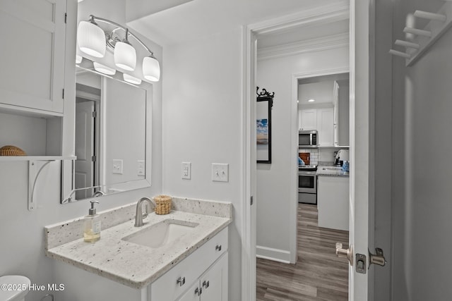 half bathroom with ornamental molding, wood finished floors, vanity, and baseboards