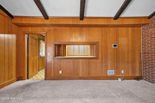 carpeted empty room featuring a textured ceiling, beam ceiling, and wood walls