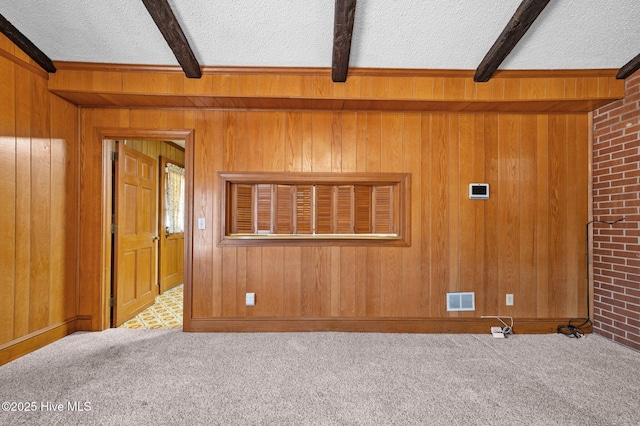 carpeted empty room featuring wooden walls, a textured ceiling, and beam ceiling