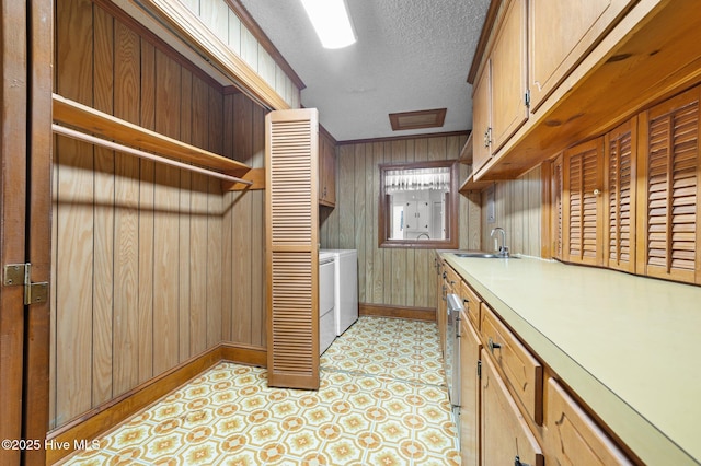 kitchen with sink, washer and clothes dryer, wooden walls, and a textured ceiling