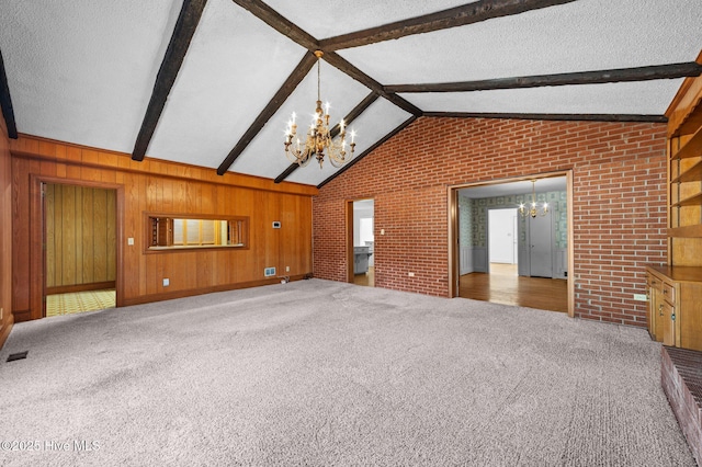 unfurnished living room with wooden walls, lofted ceiling with beams, carpet flooring, a chandelier, and a textured ceiling