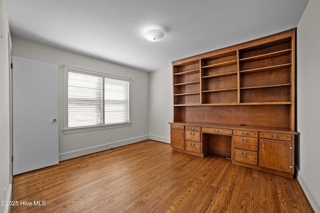 unfurnished office featuring built in desk and hardwood / wood-style floors