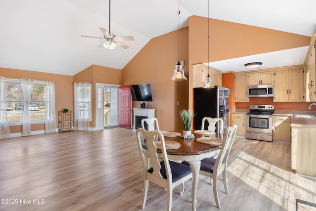 dining area featuring ceiling fan, high vaulted ceiling, sink, and light hardwood / wood-style flooring