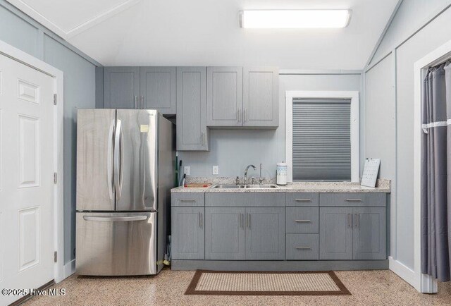 kitchen with light speckled floor, gray cabinetry, freestanding refrigerator, vaulted ceiling, and a sink