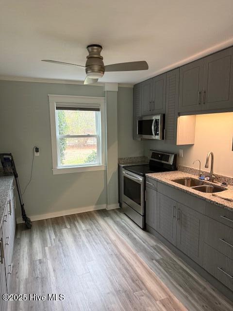 kitchen featuring a sink, baseboards, appliances with stainless steel finishes, gray cabinets, and light wood finished floors