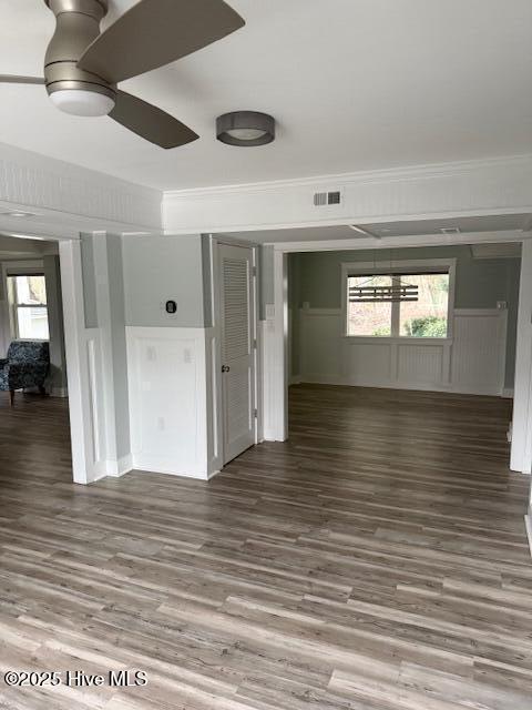 empty room with a wainscoted wall, a ceiling fan, visible vents, dark wood finished floors, and crown molding