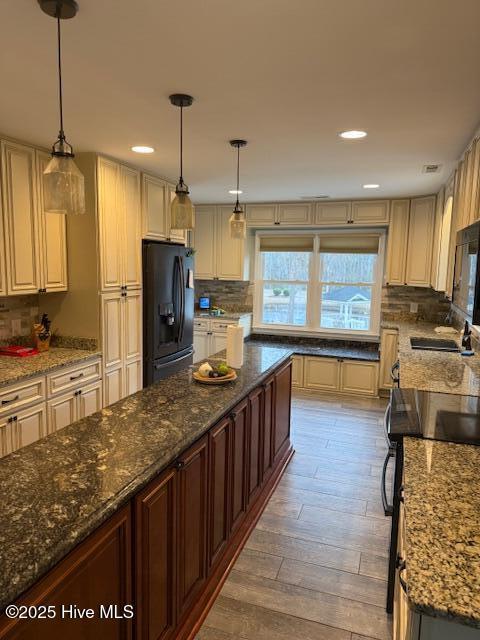 kitchen with black refrigerator with ice dispenser, a sink, decorative light fixtures, and tasteful backsplash