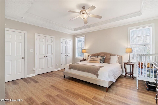 bedroom with wood-type flooring, multiple closets, ornamental molding, ceiling fan, and a raised ceiling