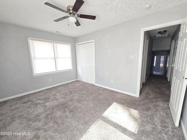 unfurnished bedroom with dark colored carpet, ceiling fan, a textured ceiling, and a closet