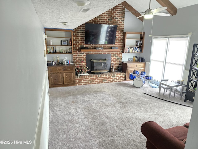 living room with ceiling fan, vaulted ceiling with beams, a textured ceiling, light carpet, and a wood stove