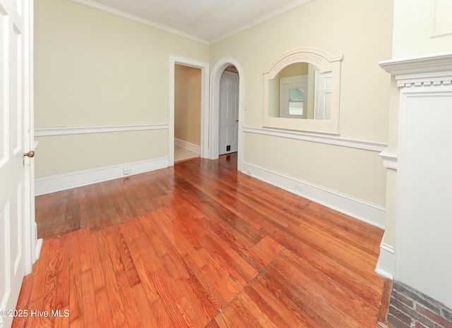 unfurnished room featuring baseboards, arched walkways, wood finished floors, and crown molding