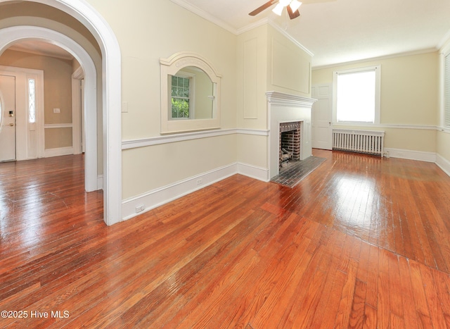 unfurnished living room with arched walkways, radiator, crown molding, and wood finished floors