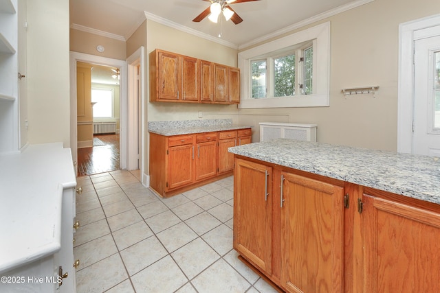 kitchen featuring brown cabinets, crown molding, light tile patterned floors, radiator heating unit, and ceiling fan