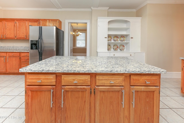 kitchen with light tile patterned flooring, a kitchen island, brown cabinets, light stone countertops, and stainless steel fridge