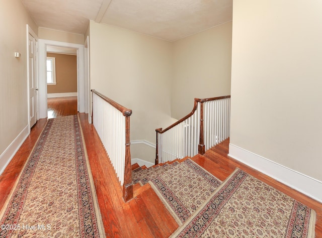 corridor with wood finished floors, an upstairs landing, and baseboards