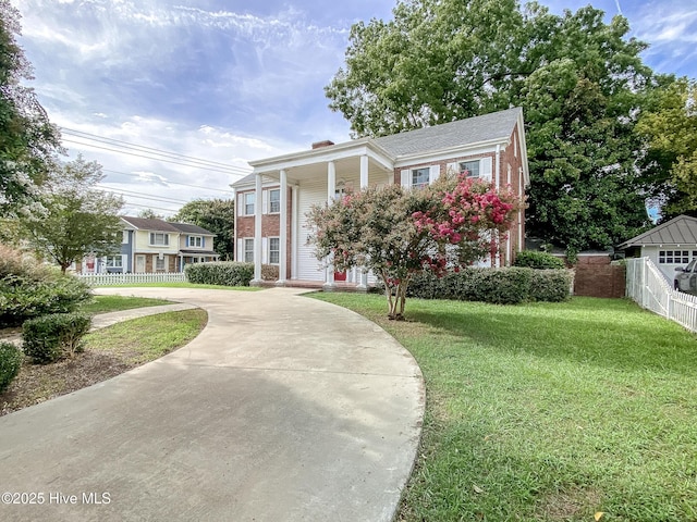 greek revival house with brick siding, a chimney, a front yard, and fence