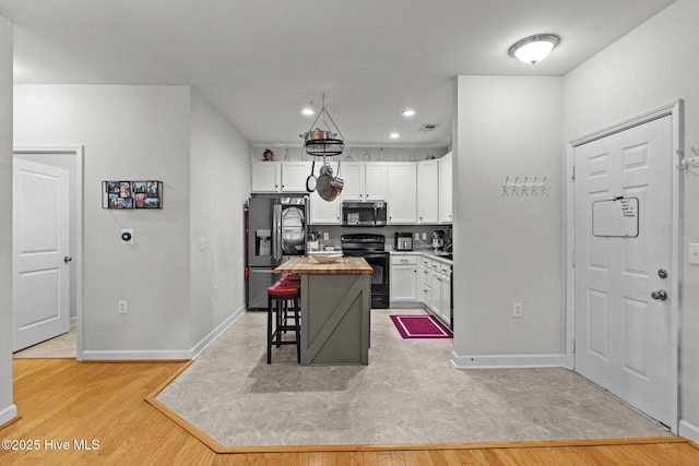 kitchen with a breakfast bar area, white cabinetry, stainless steel appliances, a kitchen island, and light wood-type flooring