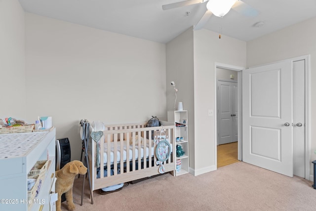 bedroom featuring ceiling fan, light carpet, and a crib