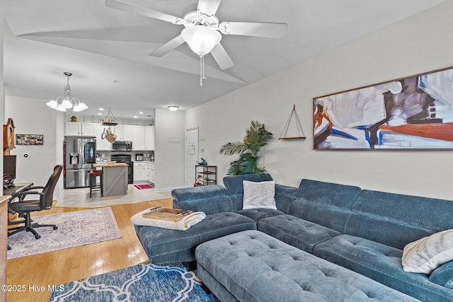 living room featuring ceiling fan with notable chandelier and light hardwood / wood-style flooring