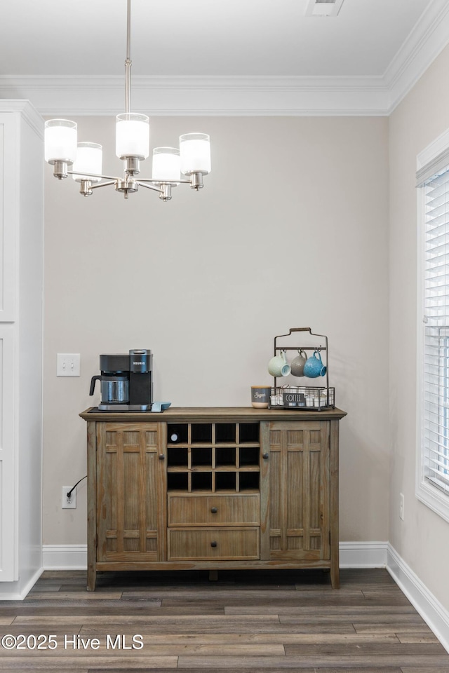 bar with hanging light fixtures, ornamental molding, dark wood-type flooring, and an inviting chandelier