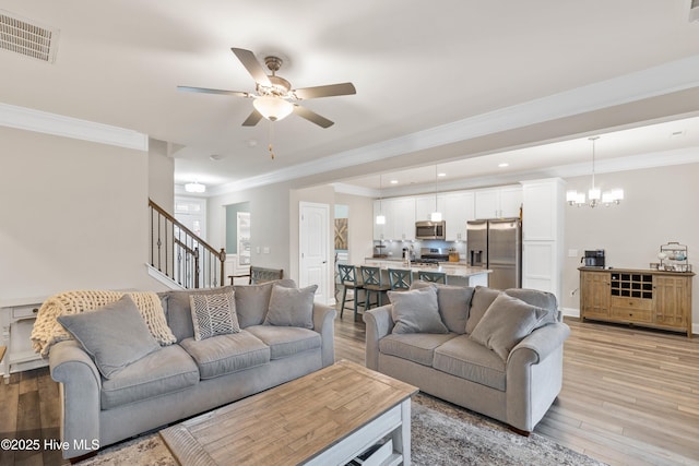 living room featuring crown molding, ceiling fan with notable chandelier, and light wood-type flooring