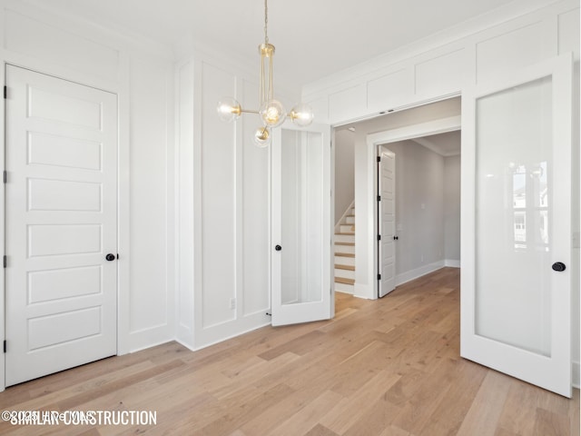 unfurnished dining area featuring a chandelier, a decorative wall, baseboards, stairway, and light wood-type flooring