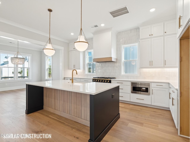 kitchen featuring a kitchen island with sink, light countertops, white cabinetry, and custom range hood