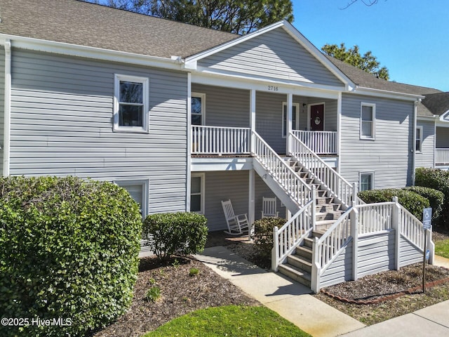 view of front facade featuring covered porch, roof with shingles, and stairway