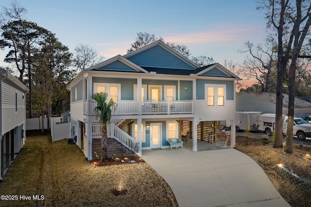 raised beach house featuring a porch, stairway, concrete driveway, and a carport