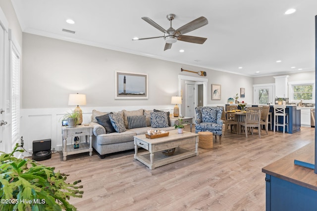 living area with recessed lighting, a wainscoted wall, visible vents, light wood-style floors, and crown molding