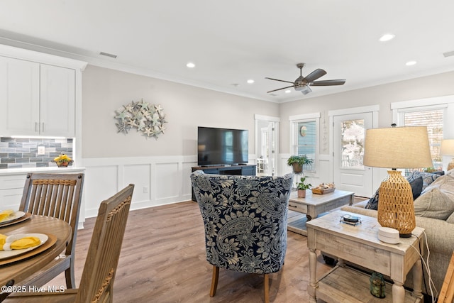 living room featuring light wood-type flooring, crown molding, a decorative wall, and recessed lighting