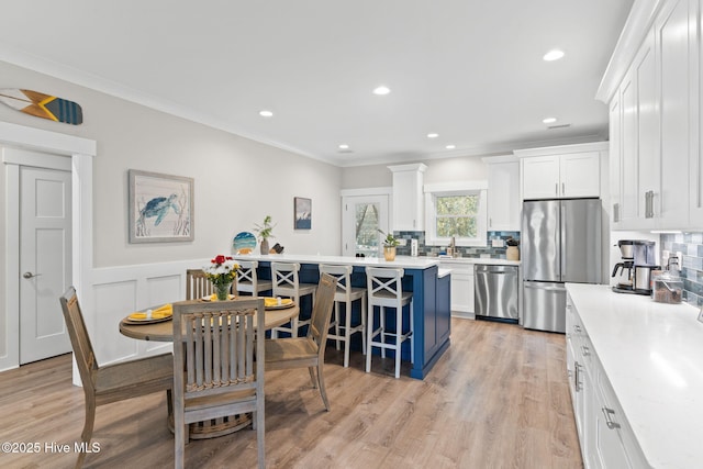 kitchen with white cabinets, appliances with stainless steel finishes, a kitchen breakfast bar, light countertops, and crown molding