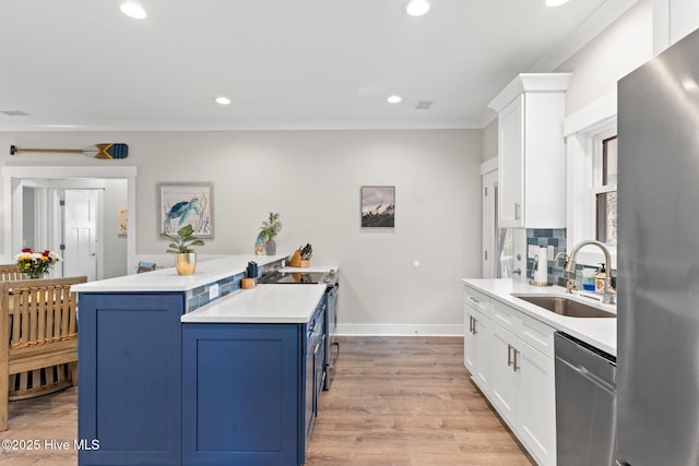 kitchen featuring appliances with stainless steel finishes, blue cabinets, light countertops, white cabinetry, and a sink