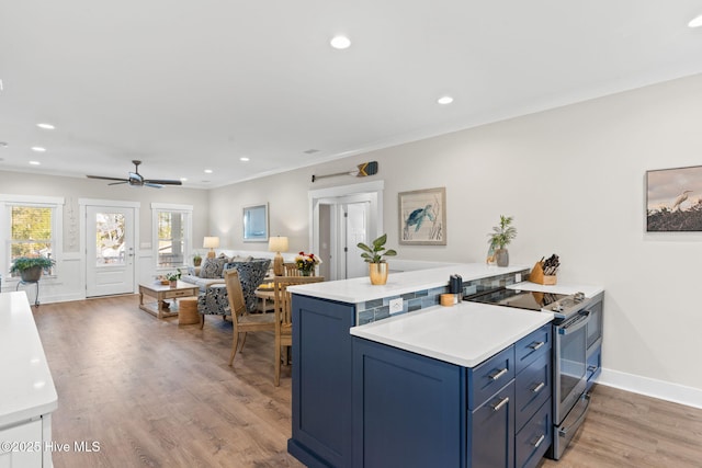 kitchen with light countertops, light wood-style floors, ornamental molding, stainless steel range with electric cooktop, and blue cabinets