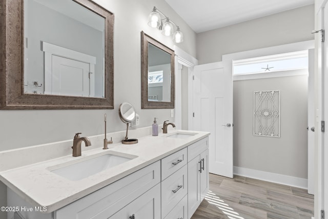 bathroom featuring wood finished floors, a sink, baseboards, and double vanity