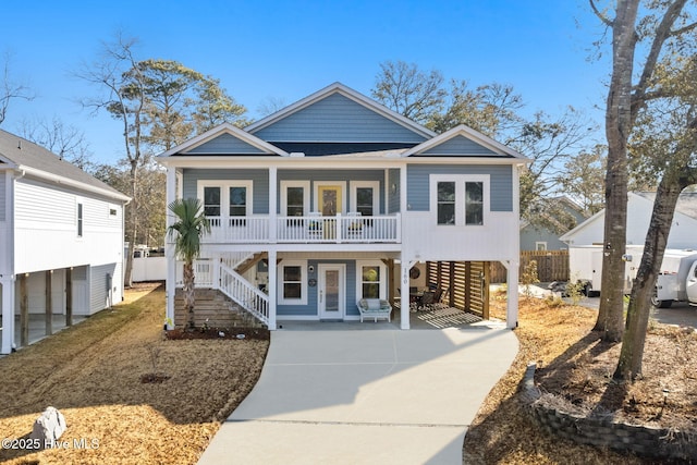 raised beach house with stairway, a porch, a carport, and concrete driveway