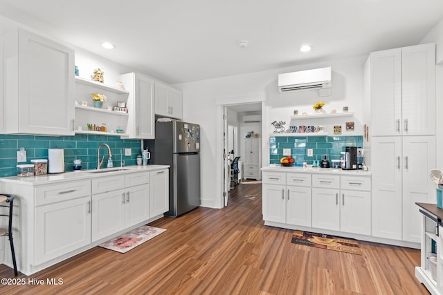 kitchen with freestanding refrigerator, an AC wall unit, white cabinetry, open shelves, and a sink