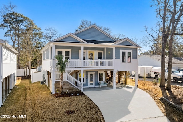 coastal home with covered porch, stairway, and concrete driveway