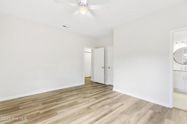 unfurnished bedroom featuring baseboards, ensuite bathroom, light wood finished floors, and visible vents