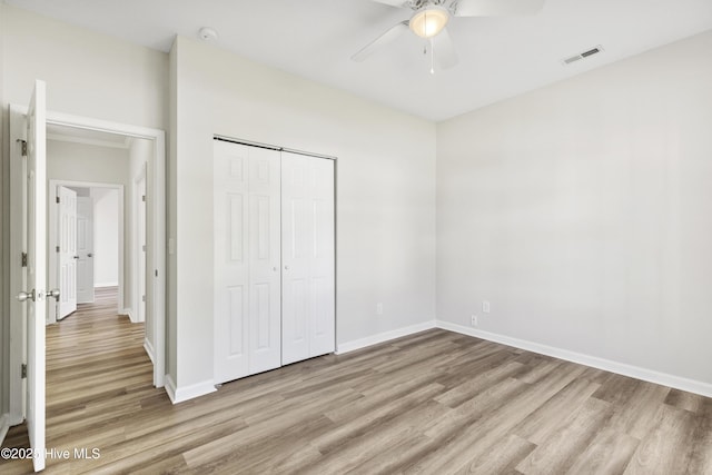 unfurnished bedroom with a ceiling fan, visible vents, wood finished floors, baseboards, and a closet