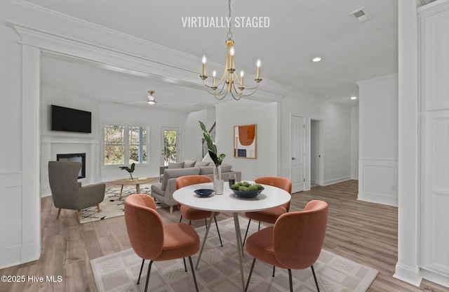 dining space featuring crown molding, a glass covered fireplace, a decorative wall, and light wood-style flooring