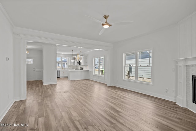 unfurnished living room featuring ceiling fan with notable chandelier, a fireplace, baseboards, light wood-type flooring, and crown molding