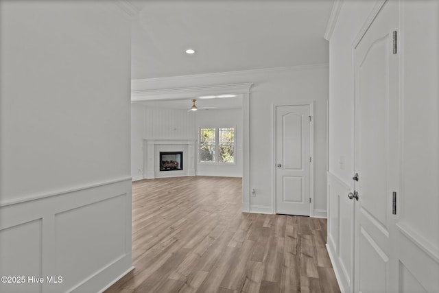 unfurnished living room with a ceiling fan, wood finished floors, crown molding, a fireplace, and a decorative wall